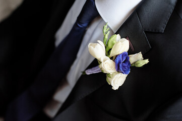 Close-up of a white and blue floral boutonniere on a suit, perfect for wedding celebration details...