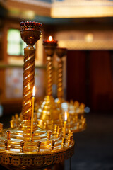 Orthodox church scene. Series of gold ornate candlesticks with lit candles, located in the serene environment of a church. Illumination adds warmth and evokes feelings of peace and spirituality.