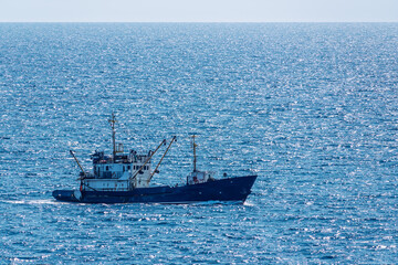 Fishing boat in blue sea and clear sky with birds flying overhead.