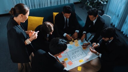 Obraz premium Top view of businesswoman write marketing idea on stick notes while standing near group of diverse people brainstorm financial strategy by using mind map. Start up team working together. Directorate.