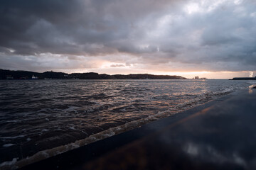 A dramatic seascape at sunset with dark clouds and choppy waves.