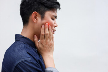 close up young asian man frown and use hand to massage on cheek after feeling pain or hurt from tmj...