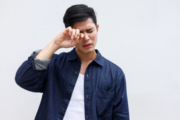 close up young man using hand to rubs eye after feeling uncomfortable sensation on white background for healthcare lifestyle concept