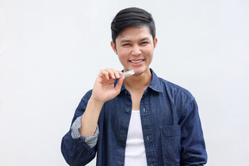 close up young asian teenager man smiling with hand holding dental aligner retainer (invisible) on white background at dental clinic for beautiful teeth treatment course concept