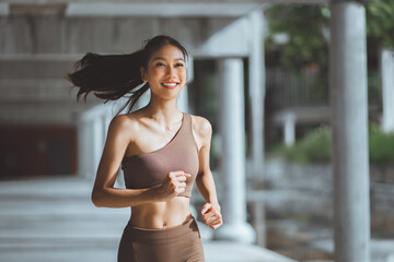 Happy asian female athlete wearing activewear running outdoors with concrete city buildings in...