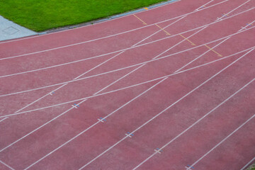Aerial perspective of red running track lanes with precise white line markings creating geometric...