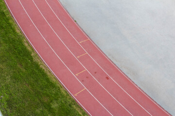 Red athletics track lanes with white markings alongside concrete surface and green field