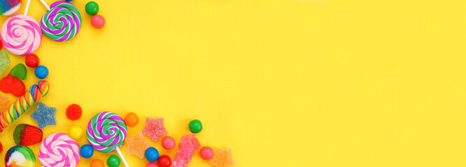 Colorful variety of candies. Overhead view corner border over a yellow banner background.