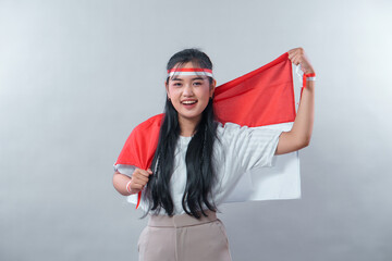 Smiling Indonesian woman proudly holding the red and white flag, wearing patriotic accessories,...