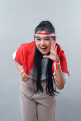 Energetic Indonesian woman in red and white accessories shouting with excitement, showing a calling...