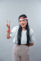 Smiling young Indonesian woman flashes a peace sign with red and white accessories, expressing joy...