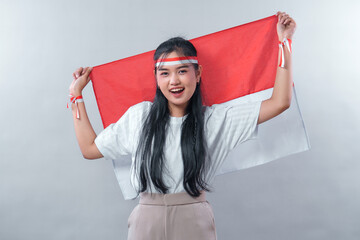 Young Indonesian woman raising the red and white flag with both hands and smiling proudly. Her pose...