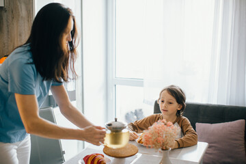 Mother pouring tea for son during breakfast at home