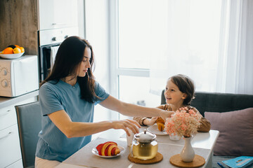 Mother giving croissant to son during breakfast in kitchen
