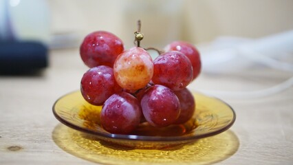 Close-up of juicy red grapes on a small glass plate, ideal for nutrition, vegan diet, and organic fruit themes