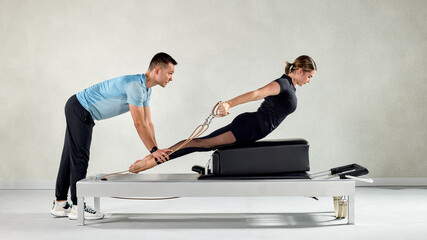 Fitness instructor assisting a Pilates session on a reformer machine