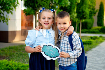 back to school. A girl and a boy schoolchildren at the school hold a sign saying It's time for school, brother and sister-first graders with briefcases rejoice at the first school day