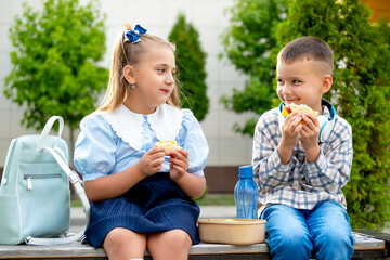 school meals, children girl and boy schoolchildren have lunch on the street with hamburgers, children brother and sister eat sandwiches before school, fast food student