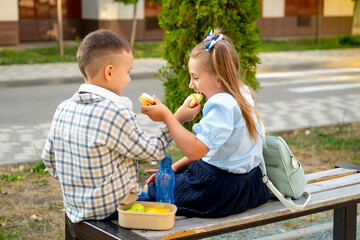school meals, children girl and boy schoolchildren have lunch on the street with hamburgers, children brother and sister eat sandwiches before school, fast food student