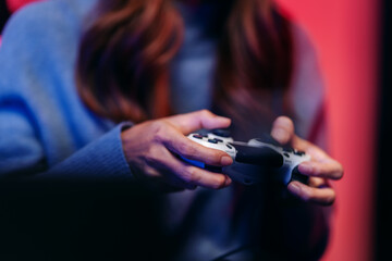 Focused gamer hands holding modern controller playing immersive video games in dimly lit room with vibrant red blue lighting for entertainment