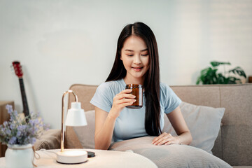 Beautiful young asian woman holding vitamin supplements jar daily healthy routine wellness self care longevity lifestyle home cozy apartment indoors