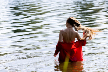 Elegant woman in red dress, back view by the lake