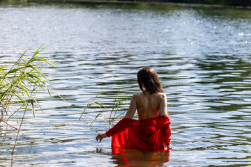 Elegant woman in red dress, back view by the lake