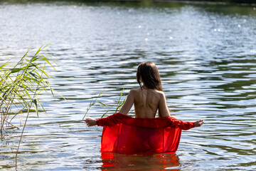 Elegant woman in red dress, back view by the lake