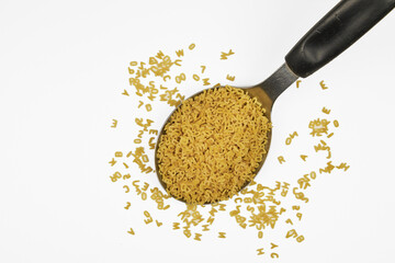 Image of raw alphabet pasta on a soup ladle, with a white background and copy space.