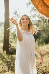 Blonde woman wearing white dress enjoying nature in sunny forest