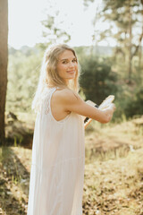 Woman holding hat smiling in nature during golden hour