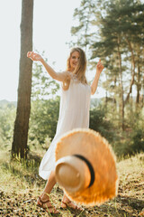 Young woman dancing in nature throwing her straw hat