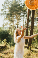 Happy young woman throwing straw hat in the air in a forest