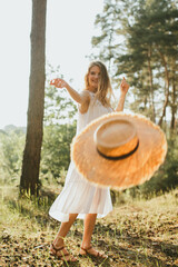 Happy woman throwing straw hat in forest sunlight