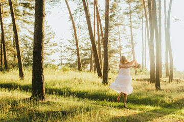 Woman dancing in forest wearing white dress at sunset