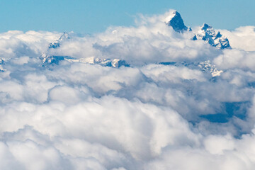 Mid-Air view of Grand Teton's jagged summit emerges above a blanket of fluffy, white clouds under a...