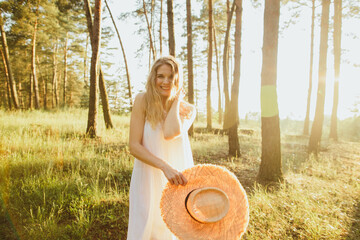 Smiling young woman holding a straw hat in a sunny forest