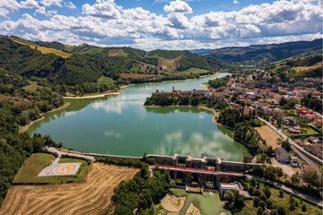 Panoramic aerial drone view of the medieval village of Sassocorvaro above the Mercatale dam, in the province of Pesaro Urbino, Marche, Italy. The village exudes peace, serenity, and ancient history.