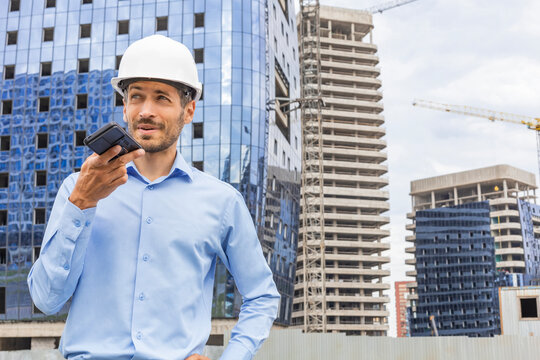 Construction engineer in helmet recording voice message while working in construction site.
