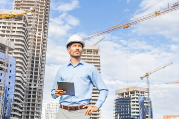 Side view of male engineer standing against background of buildings under construction working in...