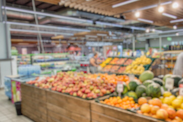 Softly blurred bokeh of a supermarket fruit section. Colorful apples, oranges, watermelons, and other fresh produce create a bright palette in the foreground.