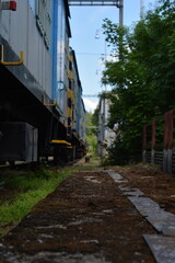 Obraz premium A low-angle shot along a railway track with a train car on the left, an overgrown path, and a blurred background, creating a sense of depth and an industrial, yet slightly abandoned, atmosphere