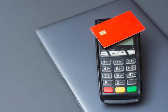 A red credit card on a payment terminal next to a laptop. Secure online transactions in e-commerce, digital payments for financial technology.