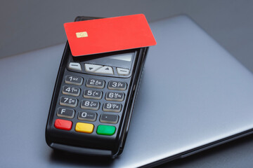 A red credit card on a payment terminal next to a laptop. Secure online transactions in e-commerce, digital payments for financial technology.