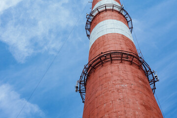 Low angle view of a tall industrial pipe with red and white stripes against a cloudy blue sky. The...