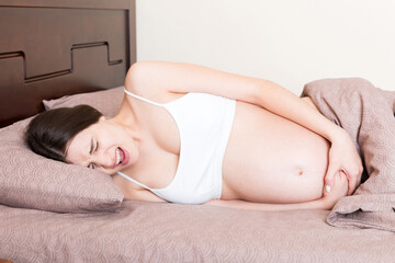 Stressed pregnant woman lying in bed with her hand on her stomach, grimacing from the bolt