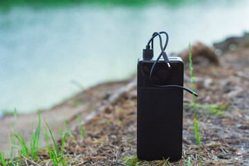 Black portable power bank with charging cable on a natural background in nature against the...