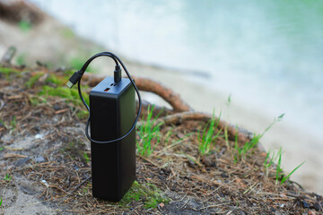 Black portable power bank with charging cable on a natural background in nature against the...