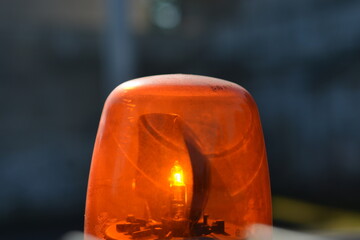 A vibrant close-up shot of an active orange emergency light, illuminating its internal bulb and casting a bright glow against a dark, blurred background, suggesting a moment of alert or warning