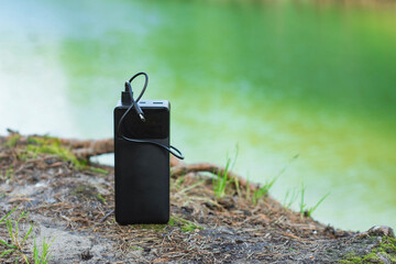 Black portable power bank with charging cable on a natural background in nature against the...